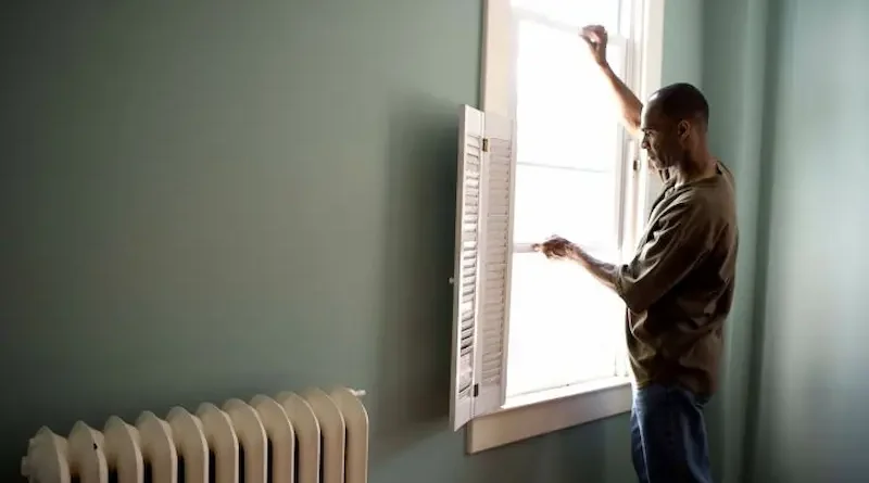 Man Adjusting Window Blinds in a Cozy Room