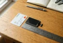 A metal ruler showing 82.51x63 mm dimensions alongside a credit card and a small touchscreen module on a wooden desk