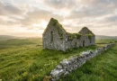 Ancient stone church ruin on a green Irish hillside surrounded by wildflowers and rolling hills under soft morning sunlight